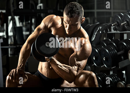 Puissance très sportif bodybuilder , exécuter l'exercice avec haltères courtes, en salle de sport Banque D'Images