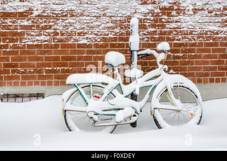 Un vélo appuyé contre un mur de briques et recouverte de neige fraîche profonde après une tempête de neige à Montréal, Canada Banque D'Images