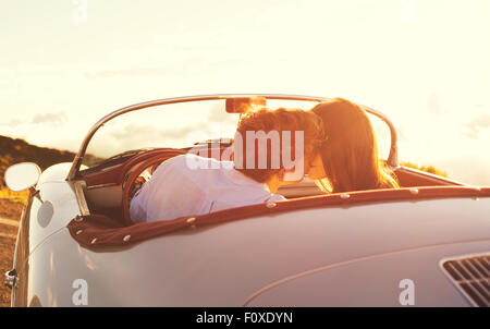 Jeune Beau couple romantique en admirant le coucher du soleil et s'embrasser dans la voiture de sport Classic vintage Banque D'Images