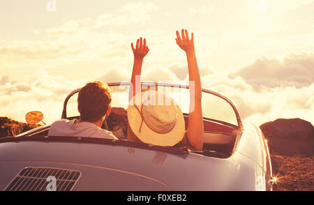 En route vers le coucher du soleil. Happy Young Couple pour le coucher du soleil dans la voiture de sport Classic vintage Banque D'Images