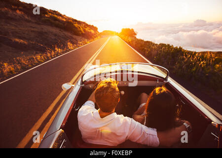 Couple heureux de la conduite sur route de campagne dans le coucher du soleil en voiture de sport Classic vintage Banque D'Images