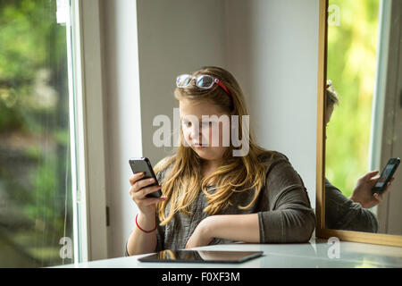 Adolescente, est assis à une table de la saisie sur un smartphone. Banque D'Images