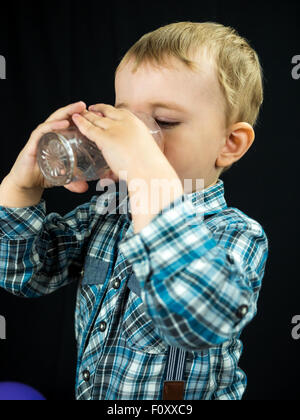 Kid boy boire du jus. Studio photo sur fond noir Banque D'Images