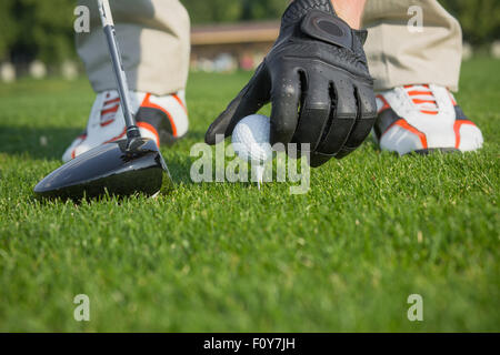 La main des hommes en cuir fendu gant en plaçant un tee avec balle de golf isolé sur fond de champ vert. Balle de golf et le bâton avec le golfeur Banque D'Images