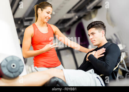 Belle jeune femme demandant à un jeune homme dans la salle de sport et d'entraînement sur son Banque D'Images