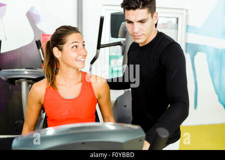 Belle jeune femme chargé par un bel homme dans une salle de sport tout en utilisant un vélo Banque D'Images