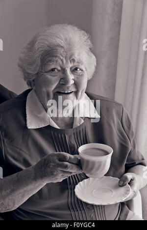 B&W image conversion RVB heureux heureux hauts vieille dame âgée assis à la maison avec une tasse de thé. Banque D'Images