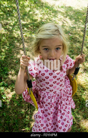 Smiling blonde enfant girl sitting in tree swing, été, Jardin, cour arrière Banque D'Images