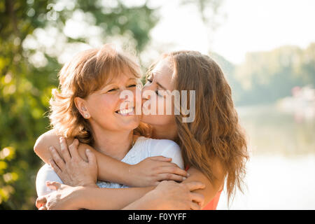 Teenage girl hugging et embrassant sa mère h piscine dans la nature aux beaux jours Banque D'Images