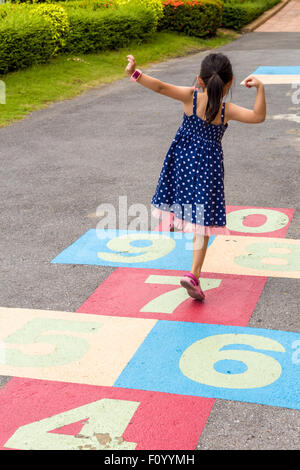 Jeune fille jouant à la marelle sur l'aire de jeux avec bonheur. Banque D'Images