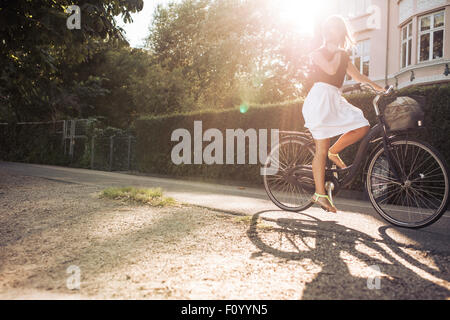 Tourné en plein air d'une jeune femme à vélo sur rue. La femme location avec sun flare. Banque D'Images