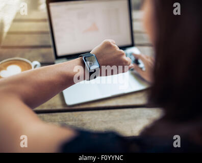 Gros plan d'une femme de vérifier de temps à sa smartwatch. Femme assise dans un café avec un ordinateur portable et une tasse de café. Banque D'Images