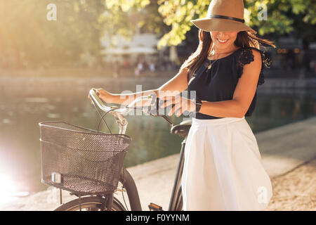 Portrait de belle jeune femme portant un chapeau avec un vélo à marcher le long d'un étang. Femme heureuse avec un vélo au parc. Banque D'Images