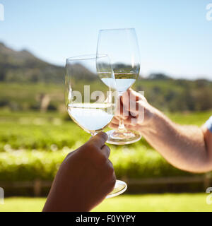 Close up of hands toasting wine à l'extérieur. Célébrer avec du vin blanc vignoble avec en arrière-plan. Banque D'Images