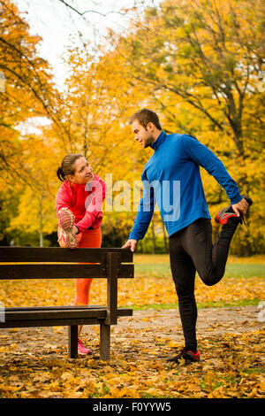 Jeune couple stretching muscles sur banc avant de jogging en automne nature Banque D'Images