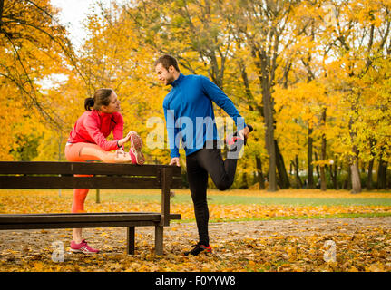 Jeune couple stretching muscles sur banc avant de jogging en automne nature Banque D'Images