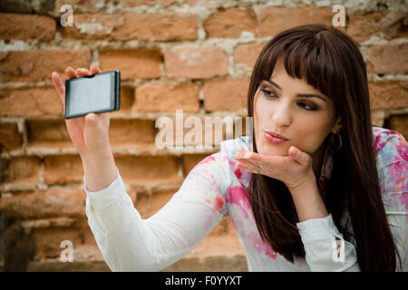 Jeune femme belle et selfies en soufflant un baiser à téléphone appareil - mur en arrière-plan Banque D'Images