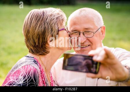 Happy senior couple taking photo d'eux-mêmes par smartphone - femme est kissing man Banque D'Images