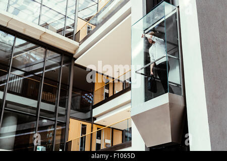 Businessman taking ascenseur en verre moderne à l''étage supérieur Banque D'Images