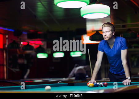 Beau jeune joueur de snooker penché au-dessus de la table dans un bar avec belle de l'éclairage ambiant Banque D'Images