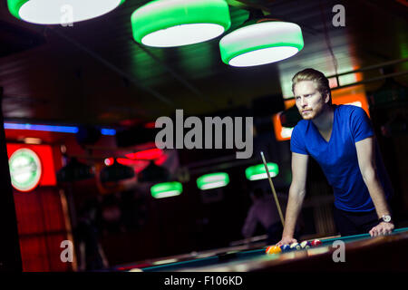 Beau jeune joueur de snooker penché au-dessus de la table dans un bar avec belle de l'éclairage ambiant Banque D'Images