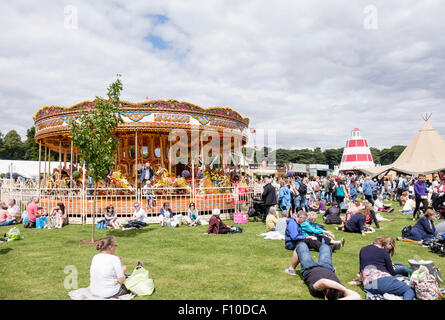 Les visiteurs assis au soleil sur les pelouses de repos par Carousel au Cheshire RHS Flower Show, le parc Tatton Knutsford Cheshire England UK Banque D'Images