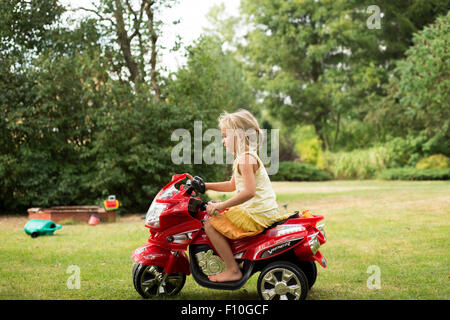 Peu de beautiful girl sitting et équitation son jouet moto électrique Banque D'Images