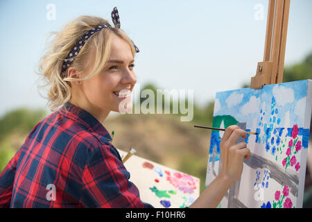 Belle blonde femme artiste peint une image colorée. Banque D'Images