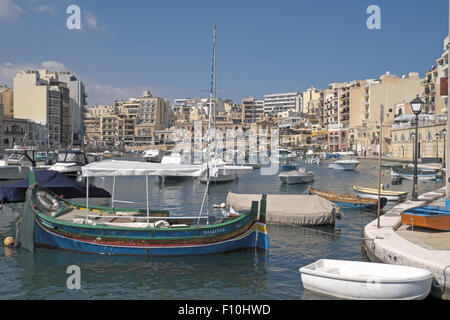 Les bateaux de pêche traditionnels peints dans des couleurs vives avec des bâtiments en pierre au-delà, St Julian's Bay (Malte). Banque D'Images