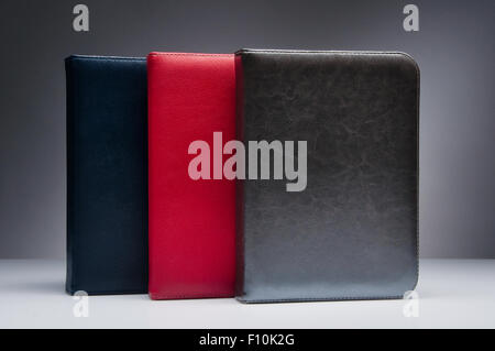 Trois ordinateurs portables avec les couvertures en cuir naturel de bleu, rouge et or-argent couleurs, debout sur la surface de la table, blanc sur noir shot g Banque D'Images