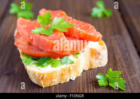 Sandwich avec le saumon (truite), fromage à la crème, la tomate et le persil sur fond en bois rustique, Close up Banque D'Images