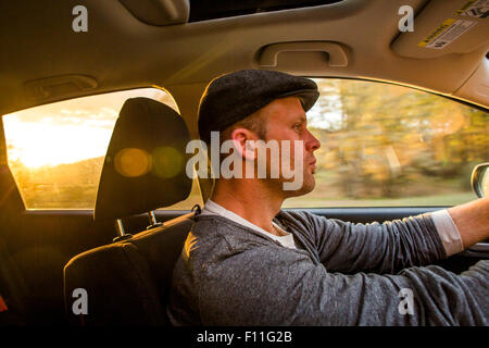 Caucasian man driving car au coucher du soleil Banque D'Images