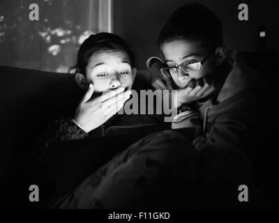 Mixed Race children using digital tablet at night Banque D'Images
