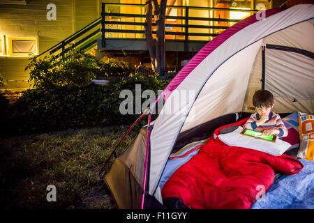 Mixed Race boy using digital tablet in backyard tente Banque D'Images