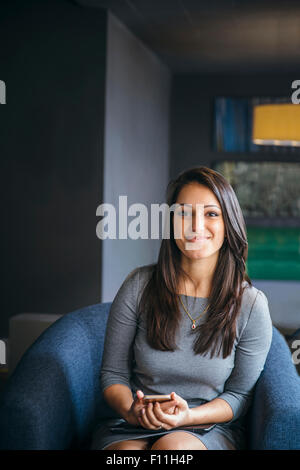 Mixed Race woman holding cell phone in office lobby Banque D'Images