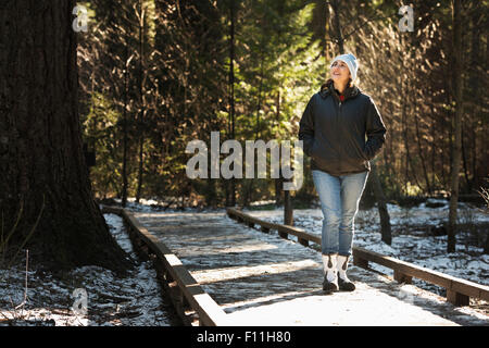 Femme hispanique sur la passerelle en bois dans la forêt enneigée Banque D'Images