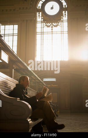 Hispanic man reading newspaper in gare Banque D'Images