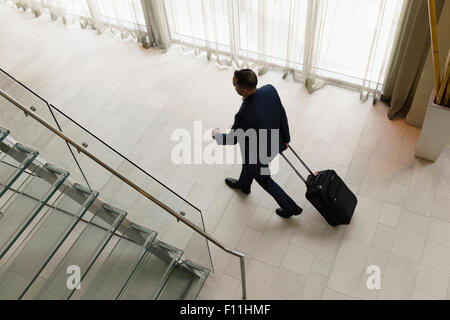 High angle view of Hispanic businessman rolling luggage in hotel lobby Banque D'Images