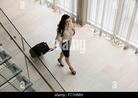 High angle view of Hispanic businesswoman rolling luggage in hotel lobby Banque D'Images
