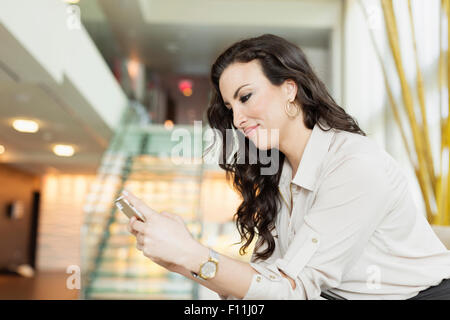 Mixed Race businesswoman using cell phone in hotel lobby Banque D'Images