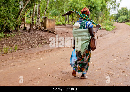 Mère portant bébé avec enveloppement traditionnel sur route de terre Banque D'Images