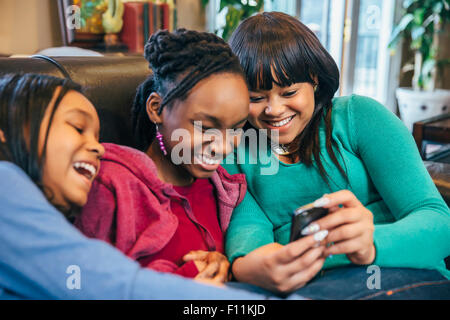 Black Sisters using cell phone on sofa Banque D'Images