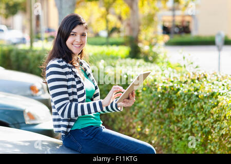 Hispanic woman using digital tablet in parking lot Banque D'Images