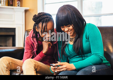 Black Sisters using cell phone on sofa Banque D'Images