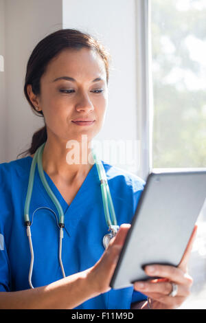 Mixed Race nurse using digital tablet at window Banque D'Images