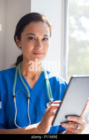 Mixed Race nurse using digital tablet at window Banque D'Images