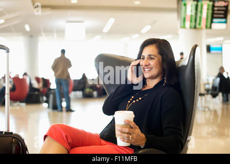 Hispanic businesswoman talking on cell phone in airport waiting area Banque D'Images