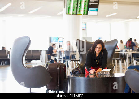 Hispanic businesswoman writing in airport waiting area Banque D'Images