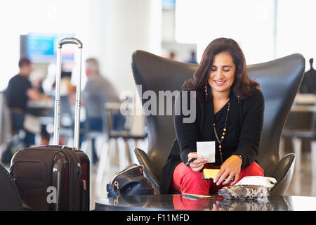 Hispanic businesswoman using cell phone in airport waiting area Banque D'Images