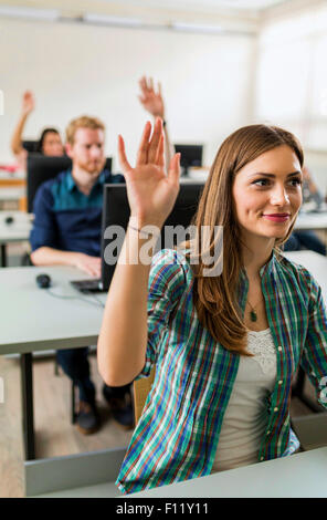 Belle jeune fille raising hand in classroom tandis qu'assis à un bureau Banque D'Images